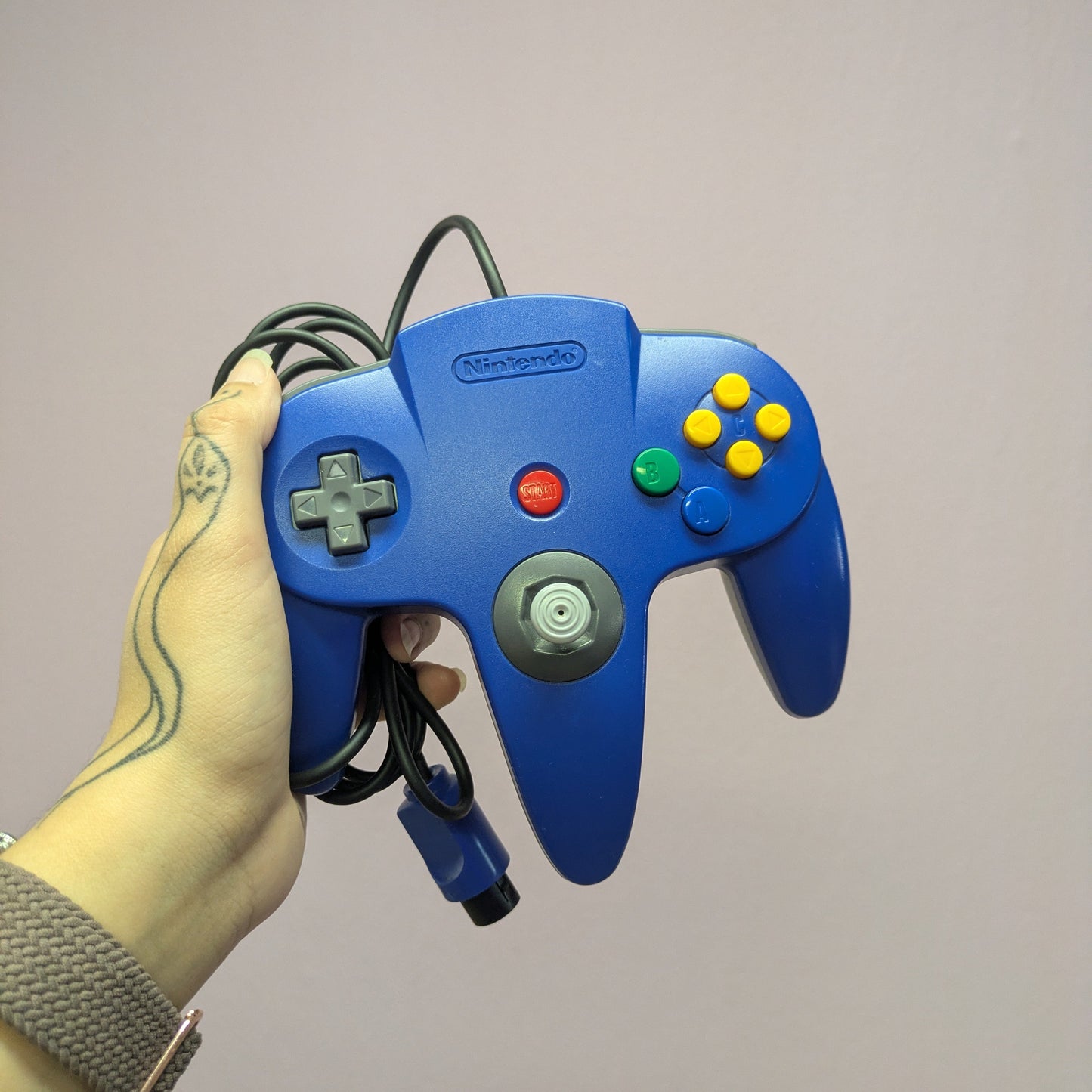 Blue Nintendo 64 controller held by a person's hand against a plain background