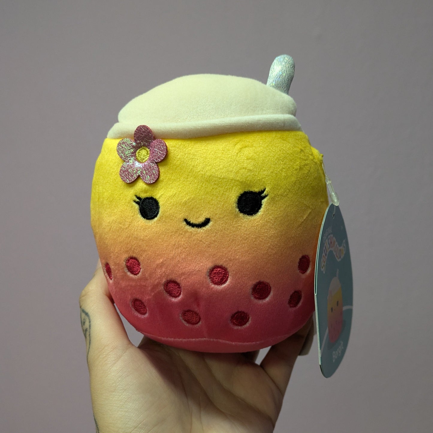 Hand holding a yellow and red boba tea plush against a neutral background
