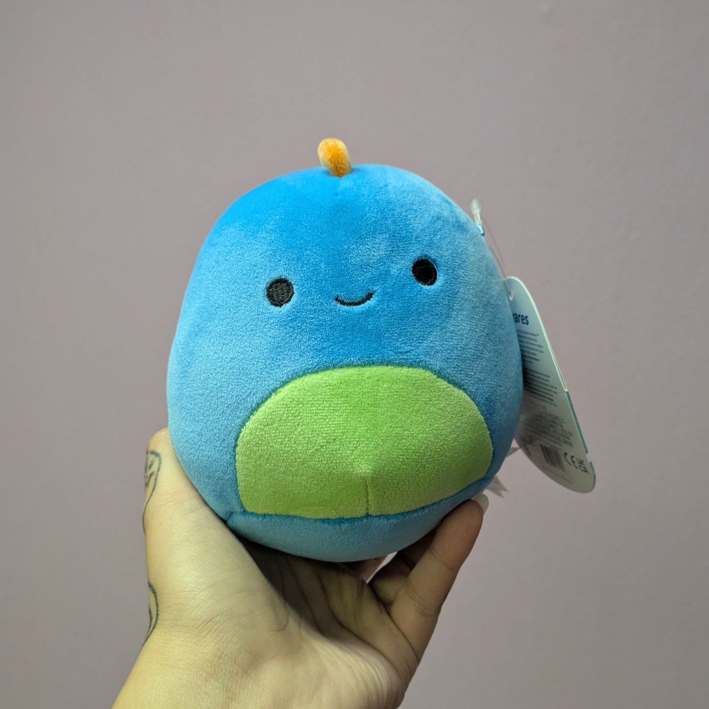 Hand holding a blue and green plush toy against a plain background