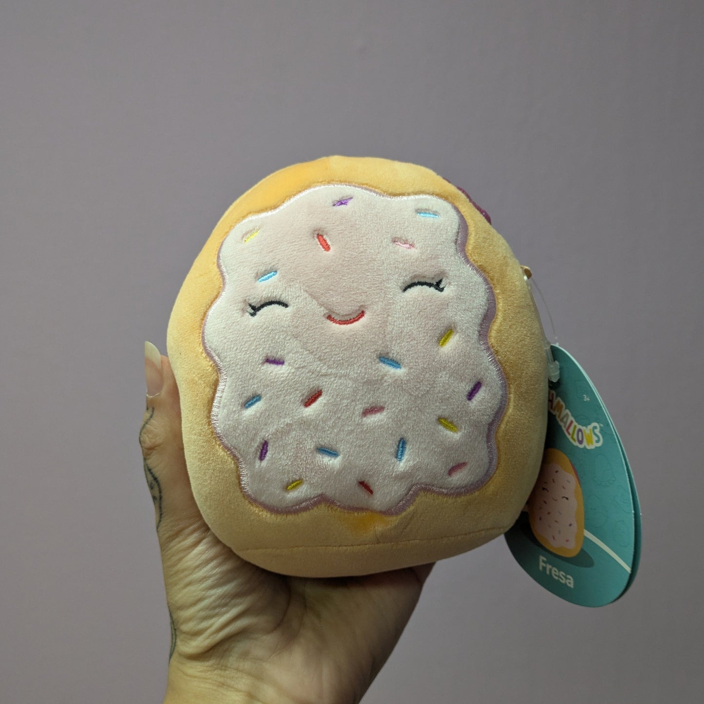 Hand holding a donut plush against a neutral background