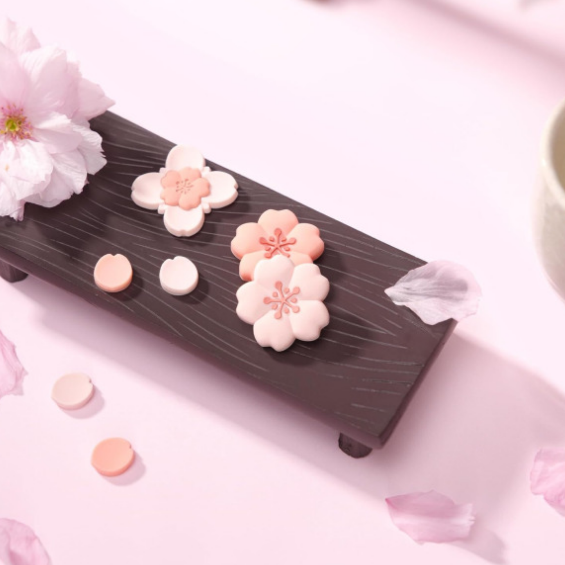 Decorative flower-shaped silicone controller grips on a faux wood stand with cherry blossoms and petals on a pink background