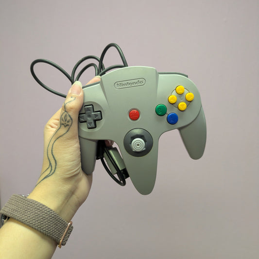 Hand holding a grey Nintendo 64 controller against a plain background