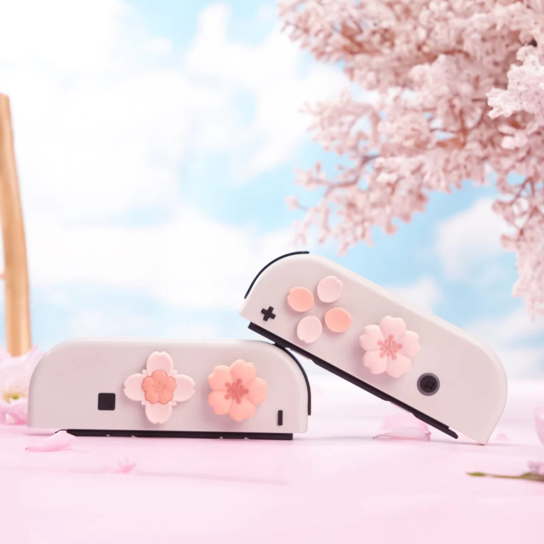 Two white gaming controllers with pink flower designs on a cherry blossom background